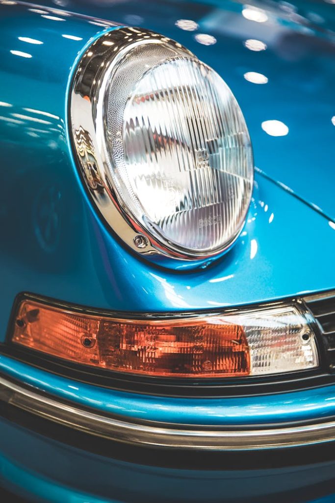 Detail of a classic vintage car headlight and bumper with blue finish and chrome elements.